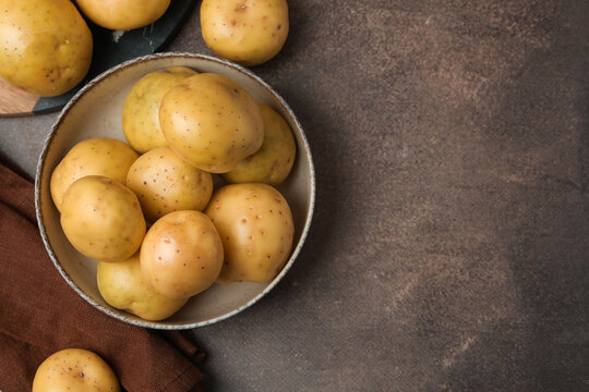 Ripe raw young potatoes in bowl and towel on brown table, flat lay. Space for text