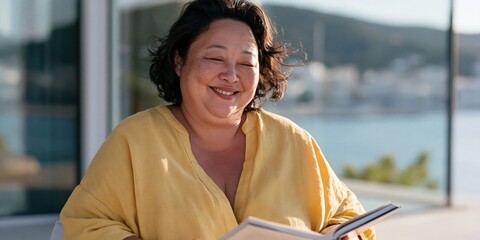 Obraz premium Joyful woman reading a book on a terrace by the sea for relaxation background and coastal lifestyle content