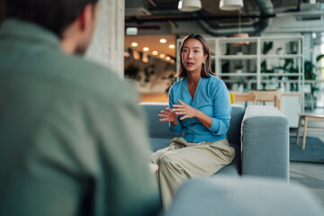Woman actively discussing and collaborating with a colleague in a modern office lounge area,...