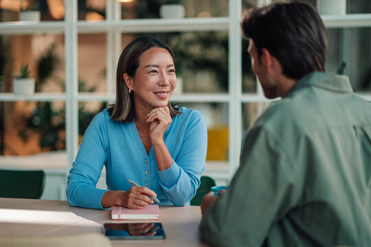 Asian businesswoman smiling, collaborating with colleague during a mentoring discussion in a modern office meeting