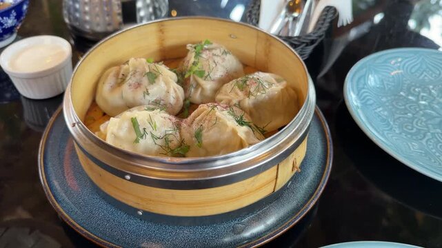 Traditional Uzbek manti, large steamed dumplings filled with meat and served in a bamboo steamer, garnished with fresh dill and herbs. Authentic Central Asian cuisine