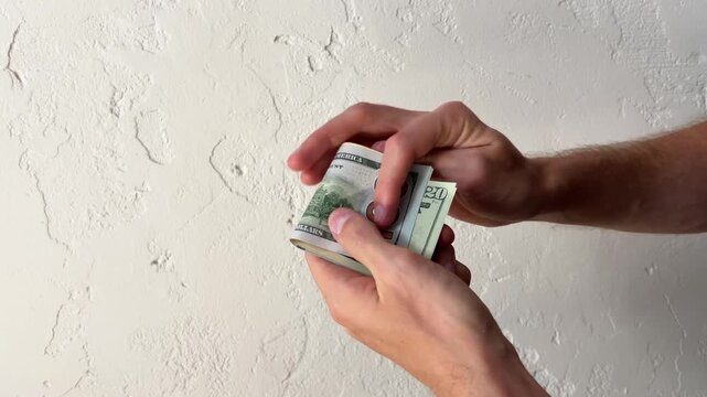 Close up of male hands holding a fan of US dollars, folding banknotes into a stack and in half against a white wall.
