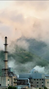 Industrial factory complex emitting thick smoke into cloudy mountain atmosphere captured in a cinematic motion video