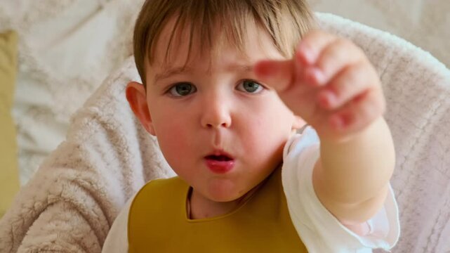The baby is happily eating fruits and berries, sitting at the table with a bib on. Kid boy aged two years (two-year-old)