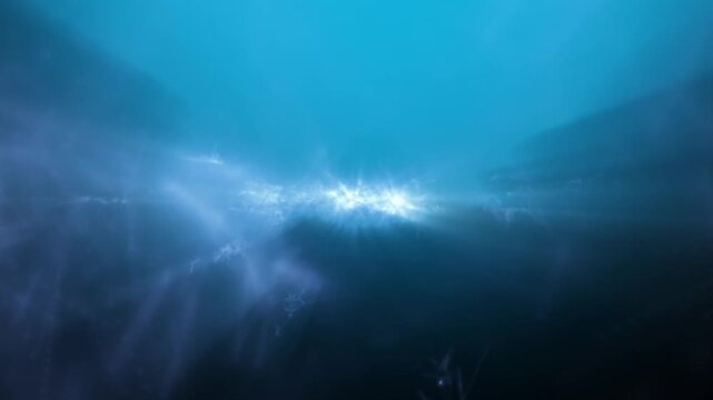 Deep underwater view with sun rays and caustic light beams shining through cloudy blue water, cinematic abstract background overlay.