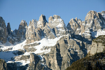 Jagged snow-dusted Dolomite peaks in Trentino rise against a clear blue sky. Rugged rock spires showcase dramatic alpine scenery. Majestic mountain landscape for travel and adventure themes. © Grenar