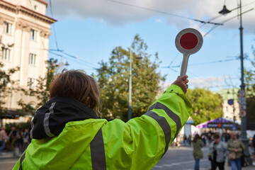 Traffic marshal directing urban traffic with a handheld stop sign, road safety and temporary traffic control. High-visibility worker signals vehicles and pedestrians on a city street © A-Quantix
