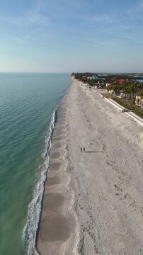 A couple walking their dogs on a nearly empty sandy beach at Casey Key, a barrier island, in Sarasota County, Florida. 