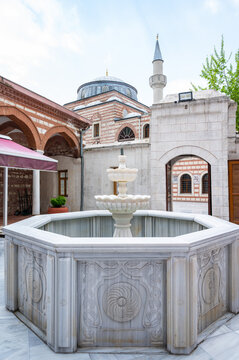 White fountain in courtyard, mosque with minaret behind, peaceful