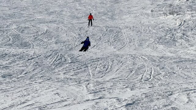 Sport man is skiing down a snowy hill. There are many people on the slope, some are skiing and others are snowboarding. The scene is lively and full of energy