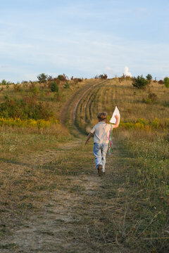Child running with a handmade kite on a country path