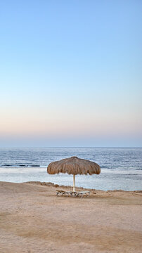 Straw beach umbrella and lounge chairs on a sandy beach at dusk.