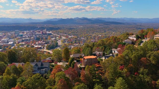 Scenic mountain community with private homes surrounded by dense woodland glowing with vibrant autumn colors. Aerial view of peaceful countryside living.