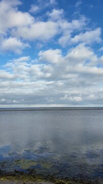 Hals, Denmark &ndash; August 25, 2026: Blue sky and puffy white clouds reflecting on the calm Kattegat sea water at Bisnap Strand