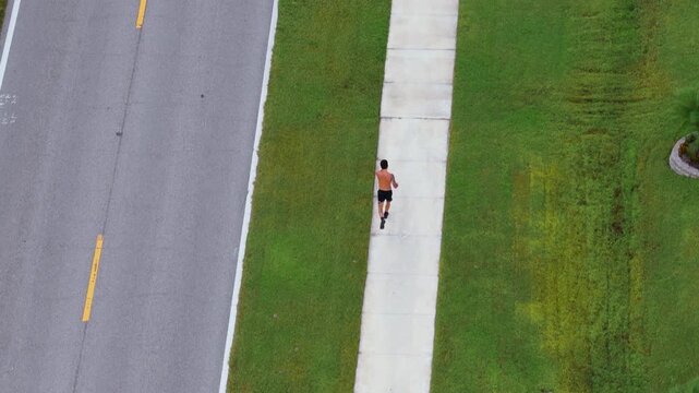 Sportsman jogging along paved sidewalk through suburban neighborhood in Florida. Outdoor running workout showing endurance, motivation and daily fitness routine.