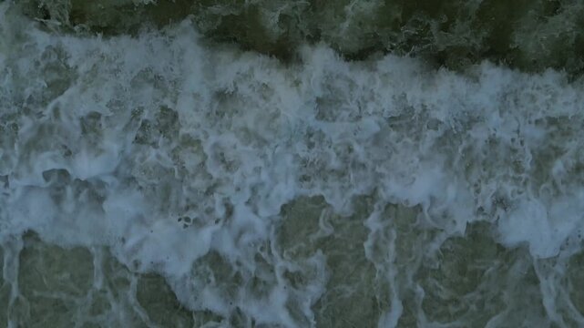 Direct overhead drone shot of turbulent river current and fast-moving white water foam