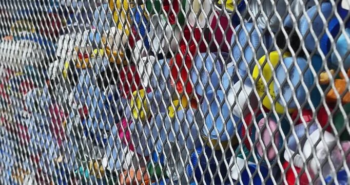 A pile of plastic caps are stacked in a cage. The caps are of different colors and sizes, recycling concept shot