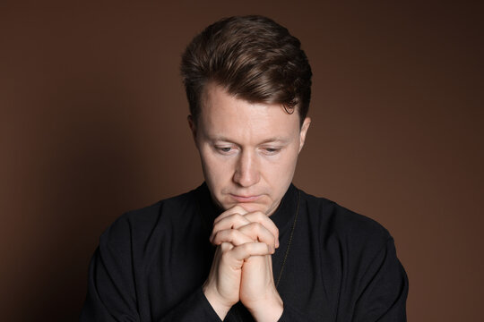 Priest in cassock praying on brown background