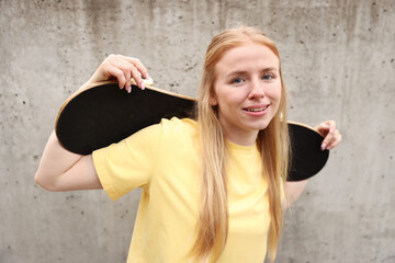 Stylish woman with skateboard near grey wall outdoors © New Africa