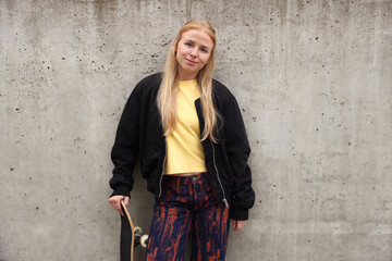 Stylish woman with skateboard near grey wall outdoors © New Africa
