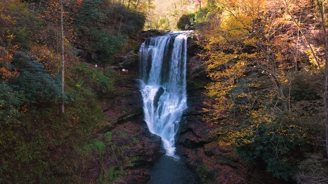 Waterfall with clear water falls behind a rocky overhang, surrounded by colorful autumn trees. Beautiful nature landscape.