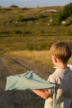 Child holding two handmade kites in a hilly landscape on a summer evening