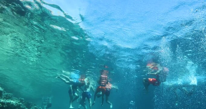 Unrecognizable people swim in life jackets in the azure sea. People in life jackets are being rescued. Tourists snorkel in the sea. Tourism and recreation concept. Underwater footage.
