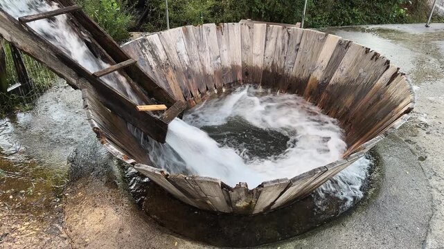 Vintage water swirl washing system. A large wooden bowl with a water flow coming out of it. The bowl is surrounded by a fence and a tree