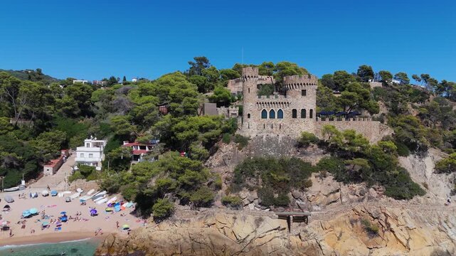 Aerial view of the coastline of Lloret de Mar, Costa Brava, Spain, filmed with a drone - the sea, beach, and castle on the coastal cliffs of the city bay on a sunny day