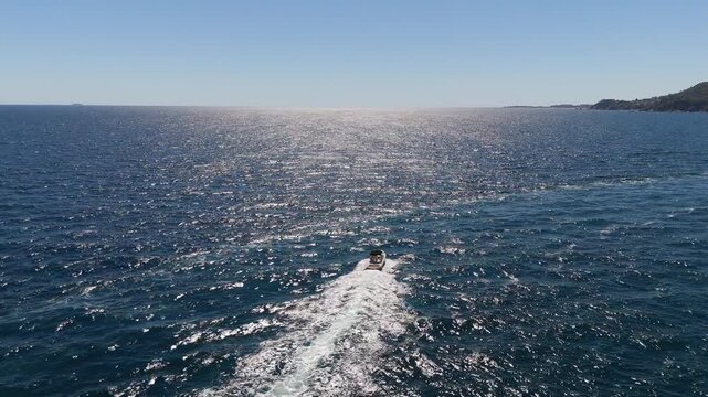 An aerial view of the Costa Brava coastline, Spain, taken with a drone, shows a boat sailing along the sea and coastal cliffs on a sunny day.