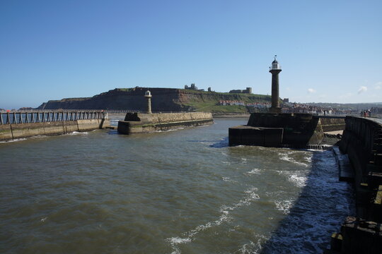 Whitby Harbour entrance showing the lighthouses, piers, and East Cliff with Whitby Abbey in the background, North Yorkshire, England