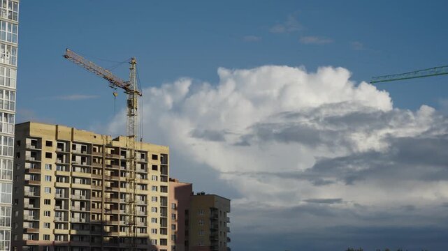 Construction cranes operate next to apartment facades under dramatic cloud formations Natural daylight creates shadows and highlights across brick surfaces and window glass Shots include close ups of 