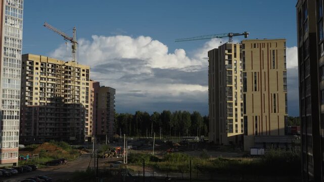 Construction cranes operate next to apartment facades under dramatic cloud formations Natural daylight creates shadows and highlights across brick surfaces and window glass Shots include close ups of 