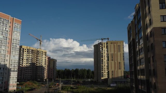 Construction cranes operate next to apartment facades under dramatic cloud formations Natural daylight creates shadows and highlights across brick surfaces and window glass Shots include close ups of 