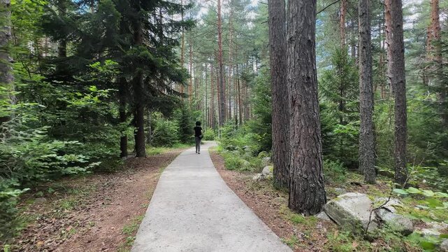 A person is walking on a path in a forest. The path is made of concrete and is surrounded by trees. The person is carrying a backpack
