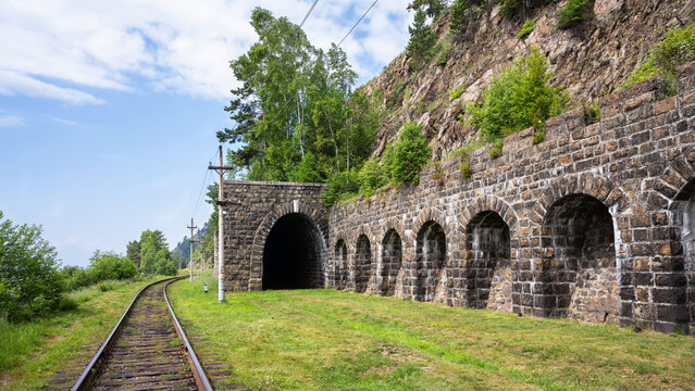 Historic stone railway tunnel and arched retaining wall at Lake Baikal, Russia. Old railroad track curving through a mountain landscape. Industrial heritage and scenic infrastructure