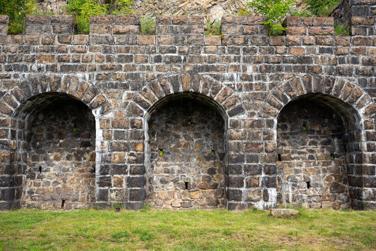 Old stone wall with three arched niches at railway station of Italian Wall at Lake Baikal, Siberia. Historic masonry structure. Weathered architecture background with green grass