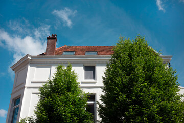 A white rendered townhouse with a moulded cornice, red roof tiles and dormer windows stands against a deep blue spring sky. © Victor
