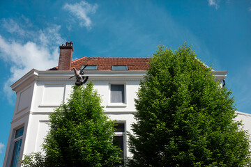 A pigeon crosses the deep blue sky beside the white rendered facade and red tiled roof of a classic townhouse. © Victor