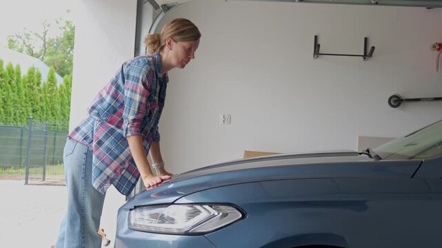 Woman closing car hood in garage after checking engine compartment
