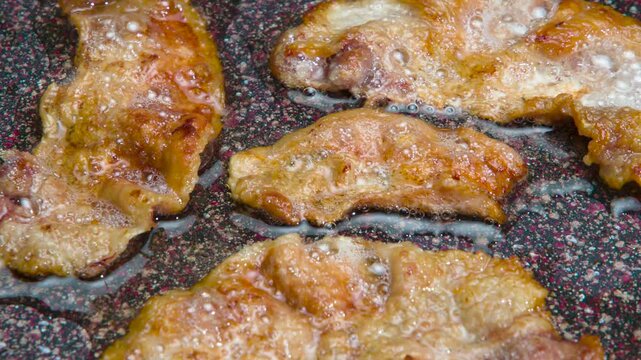 Fried Bacon Slices. Pieces of bacon fried until golden brown actively sear in hot fat