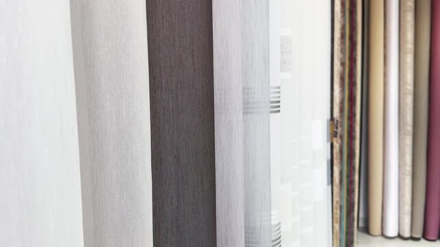 A white curtain is hanging in front of a row of brown curtains. The white curtain is the only one that is not brown