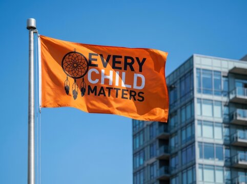 Orange flag with dreamcatcher symbol and every child matters text flies against clear blue sky background
