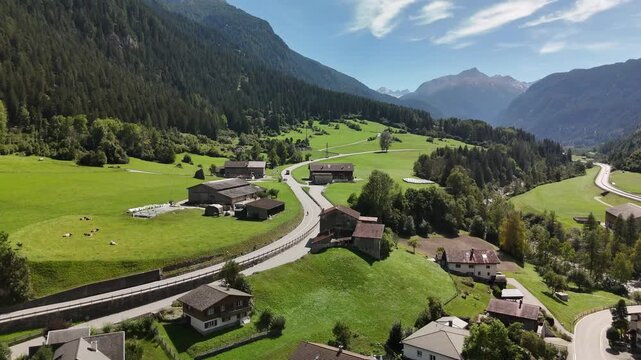 Aerial drone view of an alpine village with houses, pastures and a railway line in a green mountain valley in Switzerland