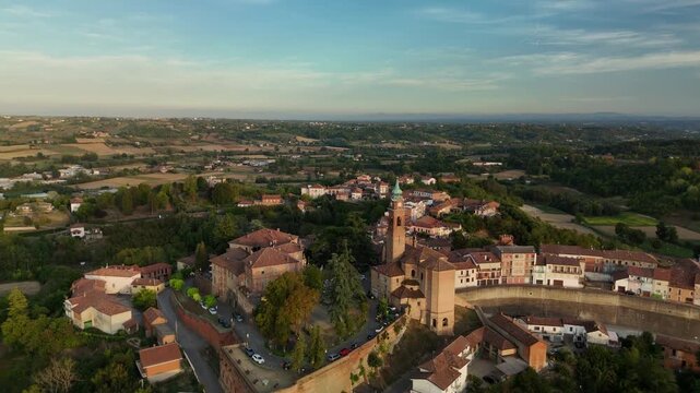 Aerial view of Castell&rsquo;Alfero medieval hilltop village with church bell tower and terracotta rooftops over Monferrato hills at sunset, Piedmont, Italy