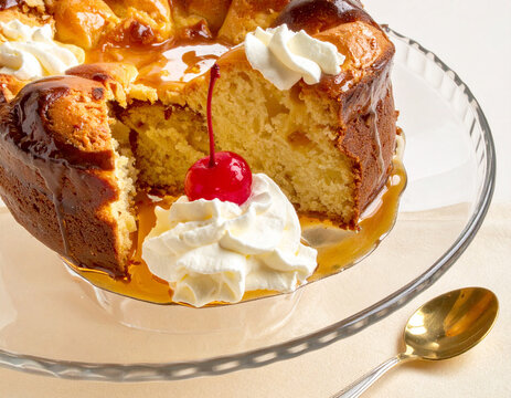 Yeast cake soaked in rum syrup topped with whipped cream and cherry served in glass bowl with gold spoon.