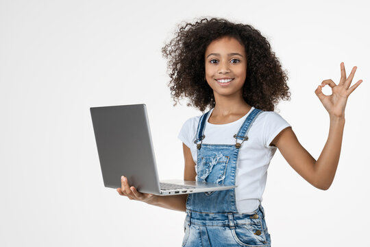 Little African girl holding laptop and making OK sign isolated on white background, smiling child with notebook computer, education, technology, online learning concept
