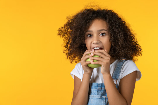 Little girl eating fresh apple isolated on yellow background, happy child enjoying healthy snack, fruit, nutrition, vitamins, organic food and healthy lifestyle concept