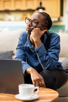 Bored African American woman with low energy sits zoned out and discouraged at home, showing lack of motivation and disinterest while struggling with monotony and feeling lazy and tired of work.