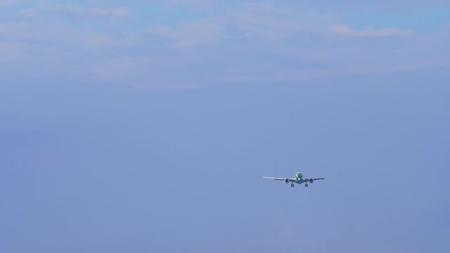 Passenger airplane descending on final approach with landing gear down against clean blue sky during daytime. Telephoto front view.